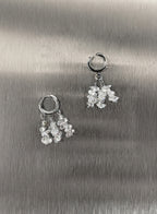 A pair of silver hoop earrings with dangling clusters of clear, faceted crystal-like beads, displayed on a brushed metallic silver surface.