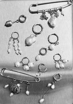 A collection of silver-toned safety-pin style earrings with dangling baroque pearl beads, arranged on a brushed metal surface.
