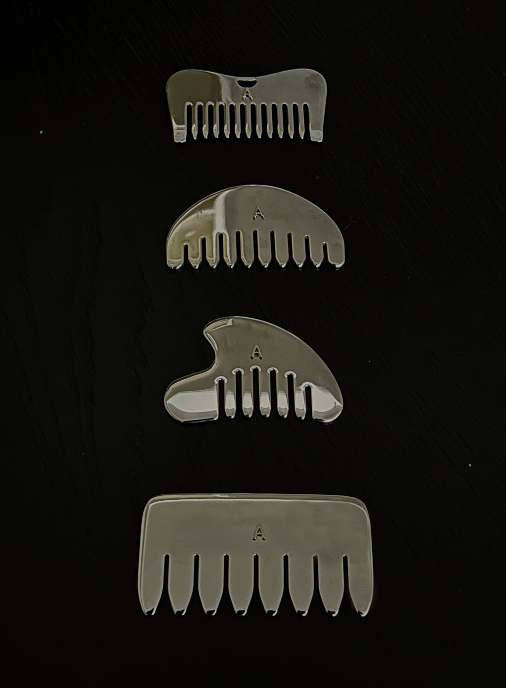 Four silver metal hair combs of varying sizes arranged vertically on a black background.