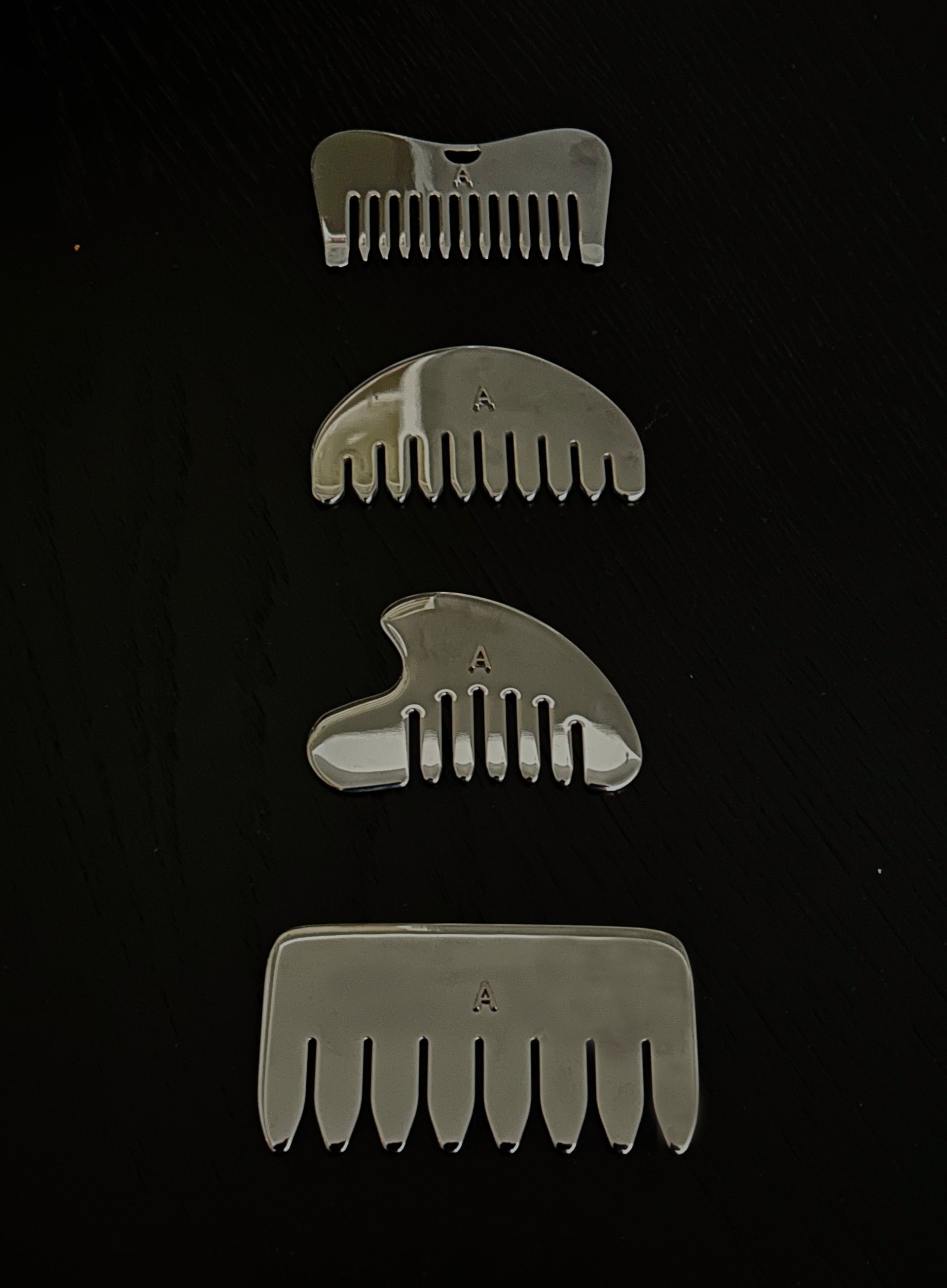 Four silver metal hair combs of varying sizes arranged vertically on a black background.