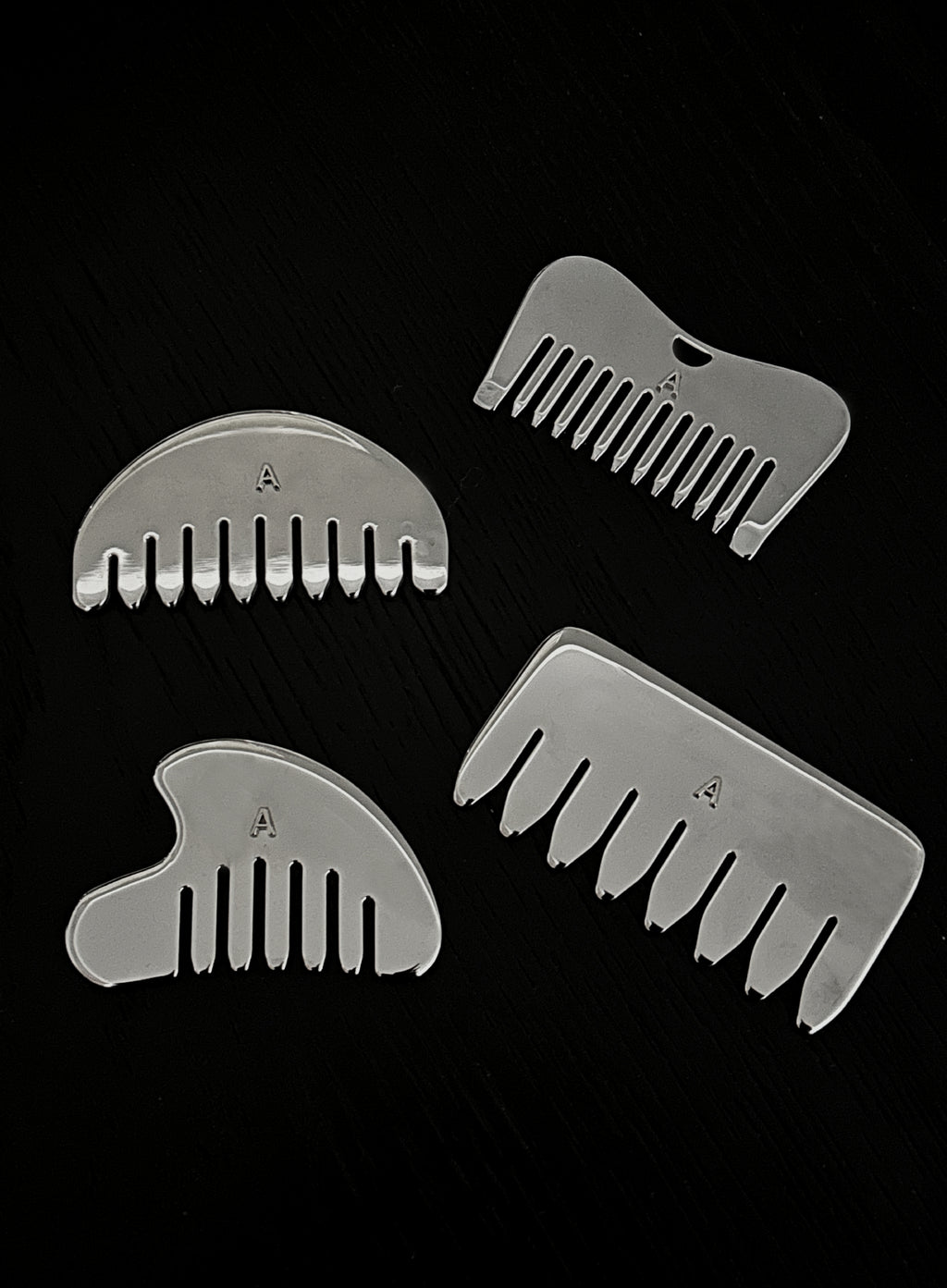Four silver metal hair-combing attachments arranged on a black background, each with a different comb shape and a small engraved letter A.