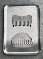 A brushed metal grooming tray containing two silver metal comb-shaped tools, each marked with the letter A, placed on a textured gray surface.