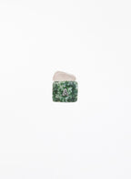 A small square gemstone charm with a green and white marbled pattern, featuring a white letter 'A' in the center, resting on a smooth, pale pink stone against a solid white background.