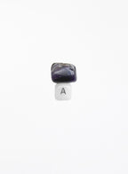 A small jewelry charm or bead featuring a polished dark purple and black stone on top of a white cube with a black letter 'A' printed on it, centered against a solid white background.