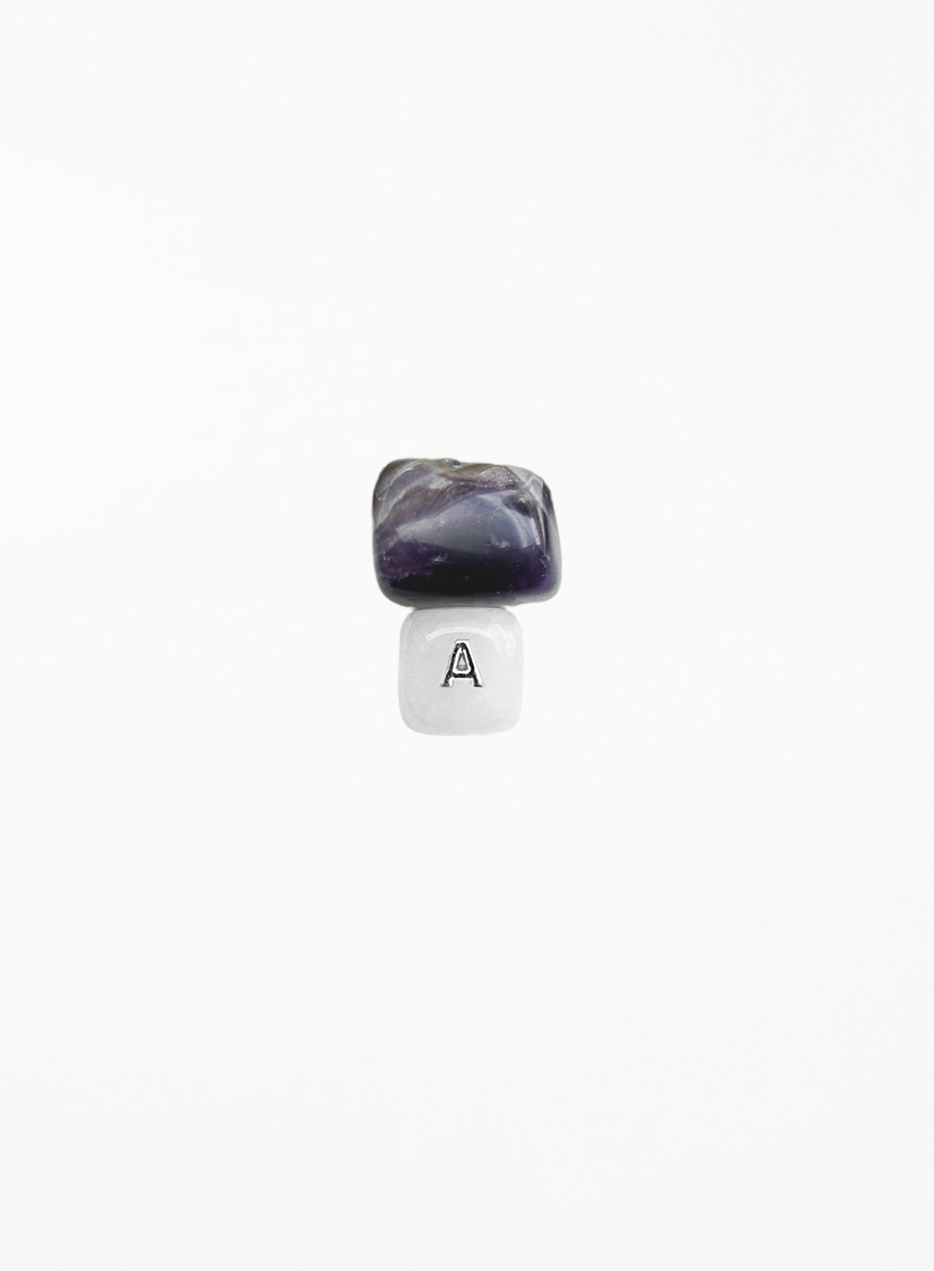 A small jewelry charm or bead featuring a polished dark purple and black stone on top of a white cube with a black letter 'A' printed on it, centered against a solid white background.