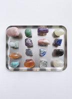 A collection of twenty different polished tumbled gemstones arranged in a grid on a rectangular silver metal tray, shot from a top-down view against a plain white background.