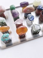 A collection of polished gemstone mushroom-shaped crsytal displayed on a silver metal tray against a white background.