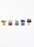 Five small polished gemstone cubes in different colors, each topped with a matching flat stone and marked with the letter A, arranged in a row on a plain white background.