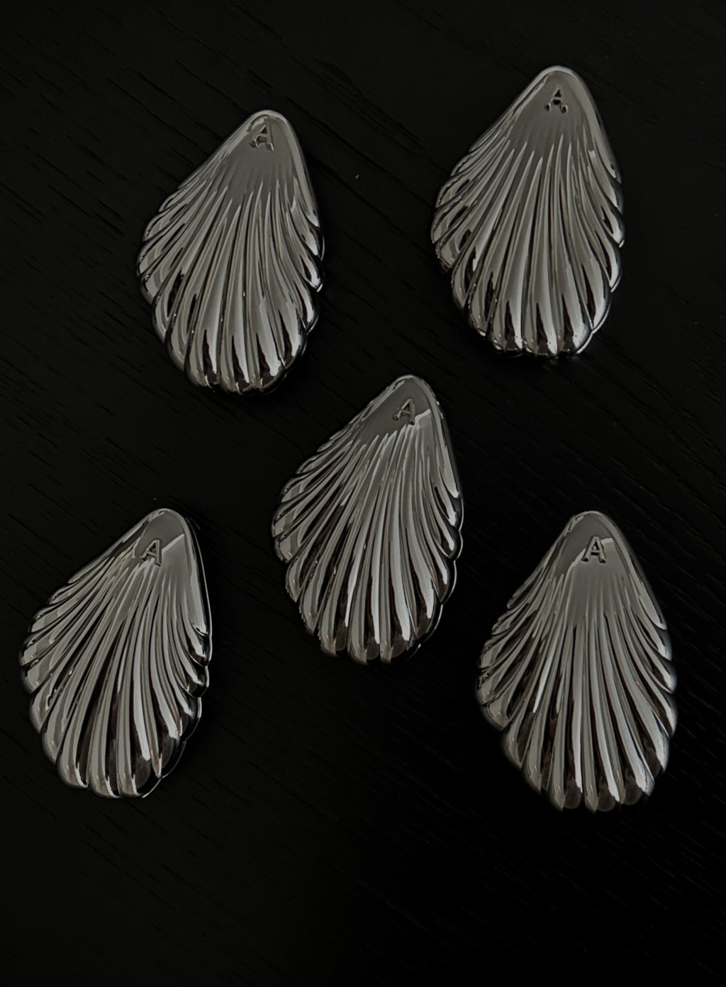 Five metallic shell-shaped jewelry pieces arranged on a dark black background.