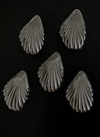 Five metallic shell-shaped jewelry pieces arranged on a dark black background.