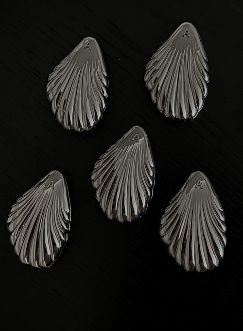 Five metallic shell-shaped jewelry pieces arranged on a dark black background.