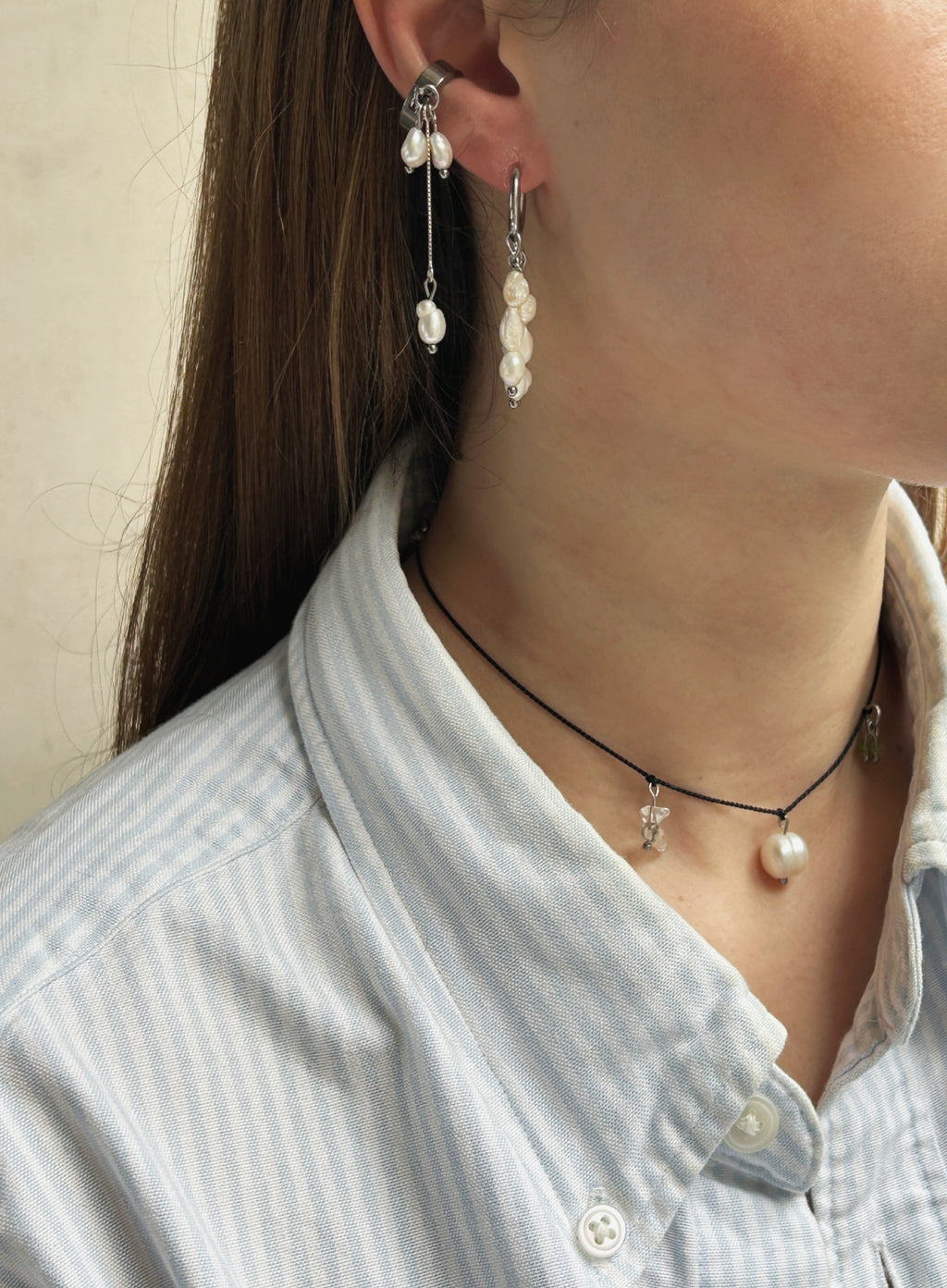 Close-up of a person wearing pearl earrings and a necklace with a neutral background