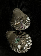 Two metallic oyster shells with various jewelry pieces on a dark surface