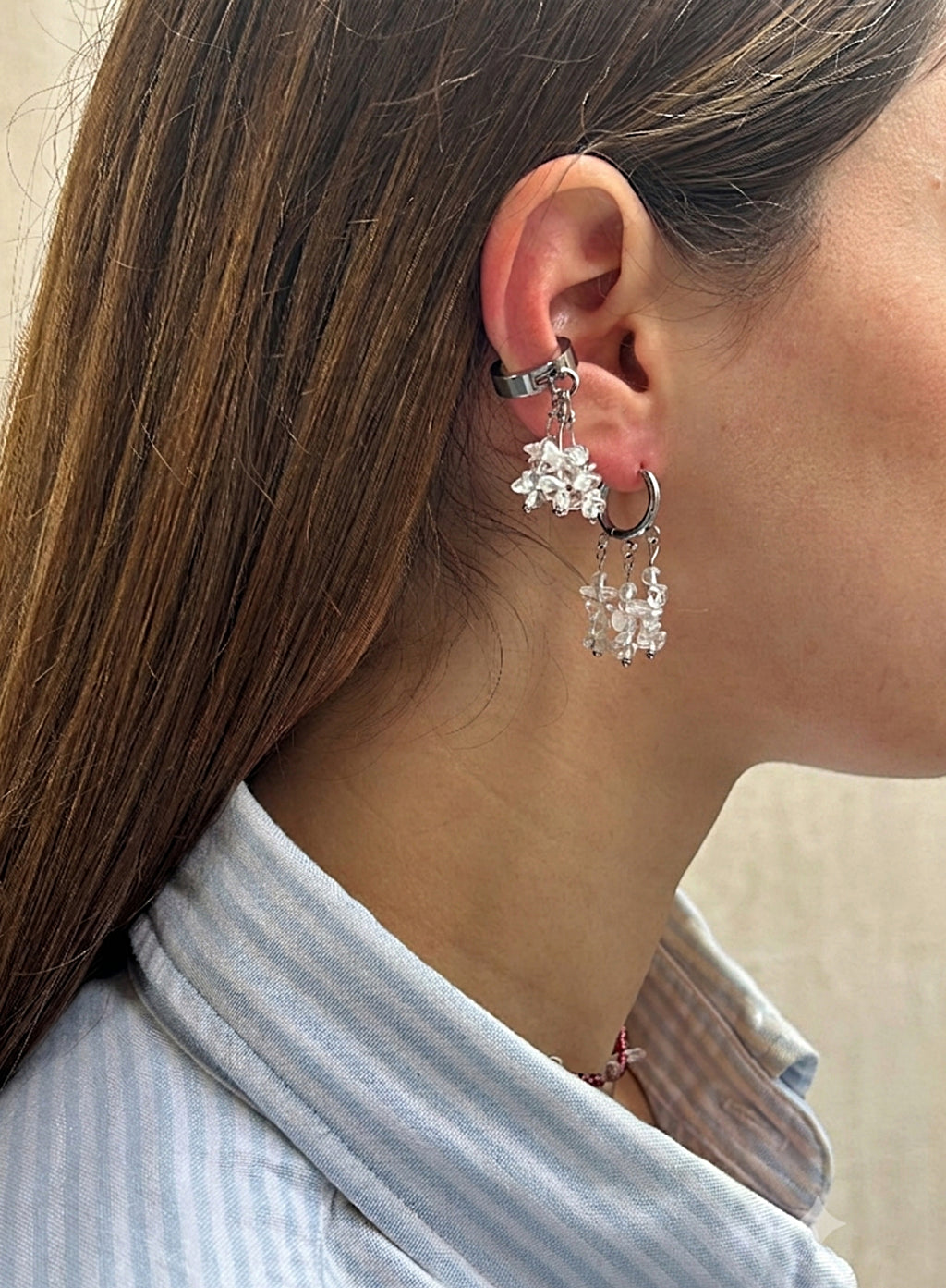 A close-up side profile of a woman wearing a silver-toned huggie hoop earring adorned with dangling snowflake-shaped crystal charms.