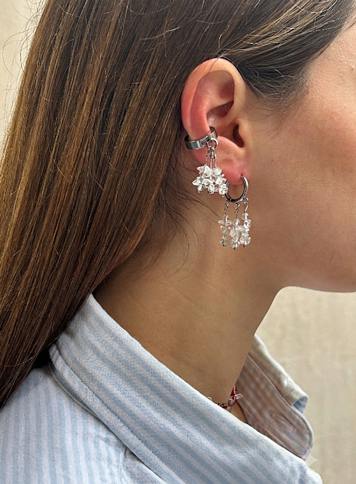 A close-up side profile of a woman wearing a silver-toned huggie hoop earring adorned with dangling snowflake-shaped crystal charms.