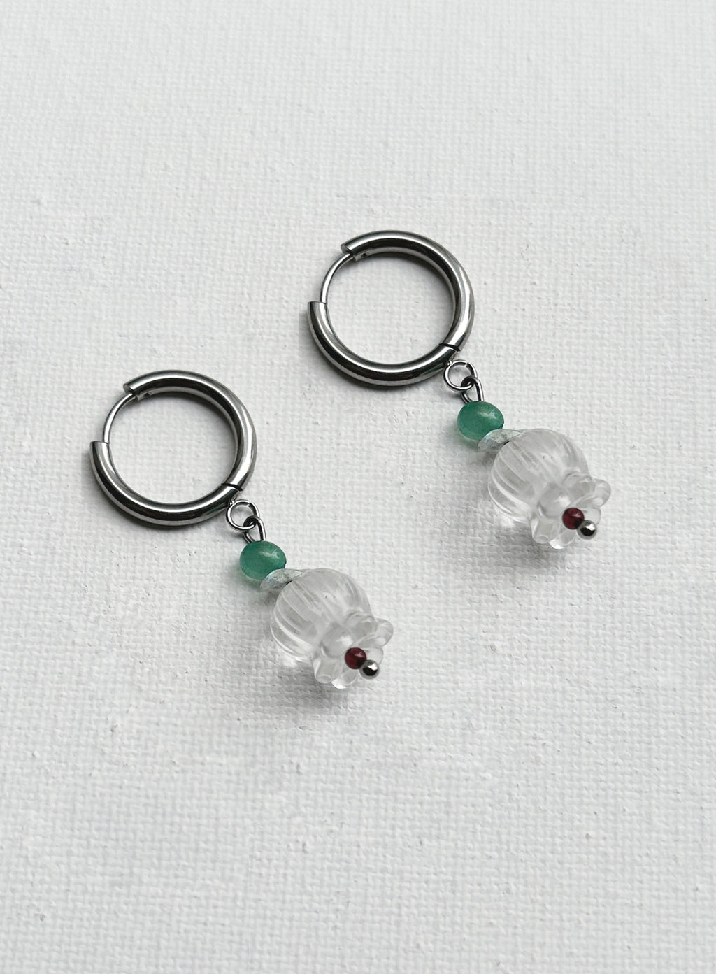 Pair of hoop earrings with clear glass beads and green gemstones on a white background