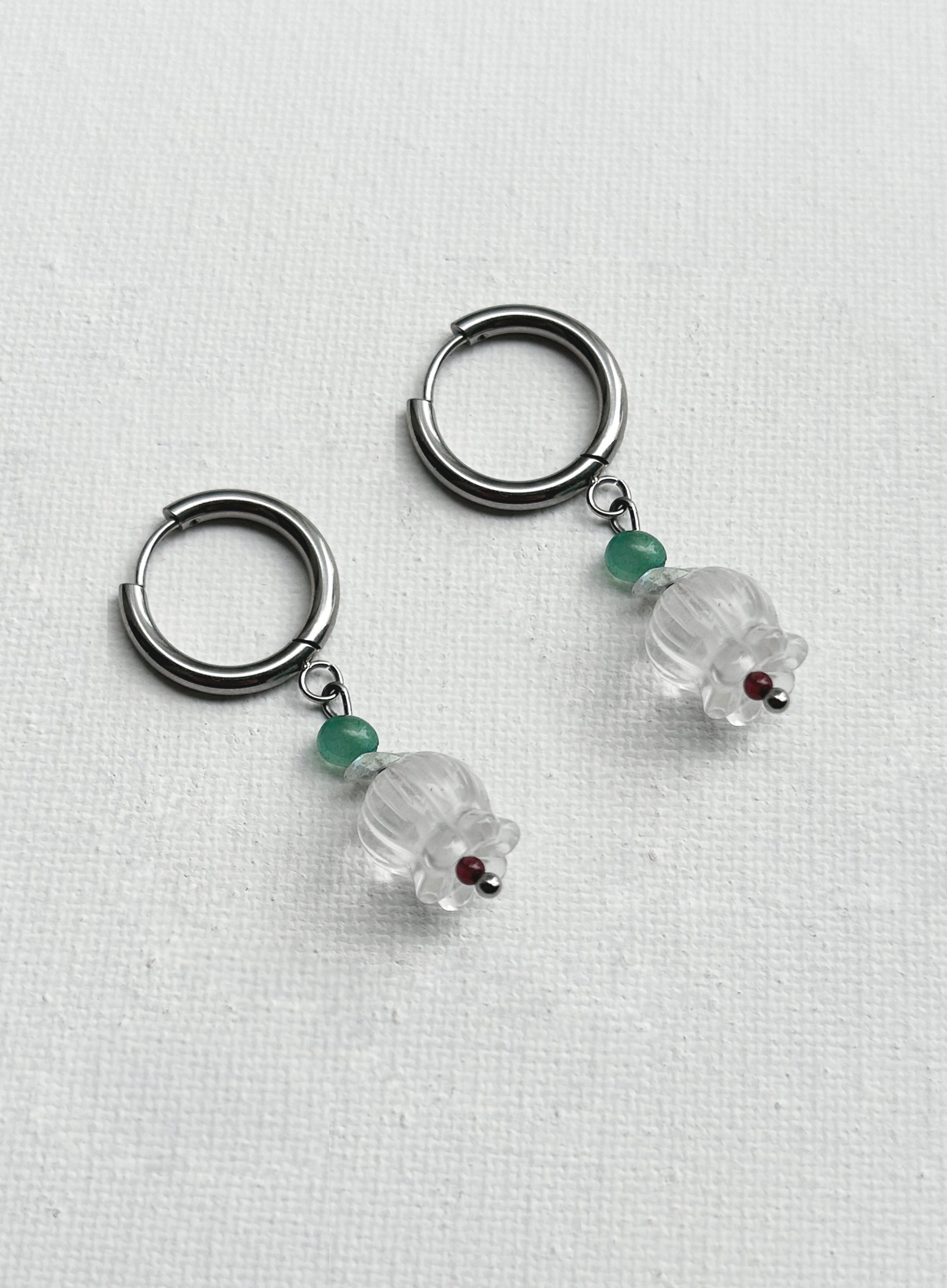 Pair of hoop earrings with clear glass beads and green gemstones on a white background