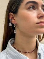 Close-up of a person wearing floral earrings and a necklace against a neutral background
