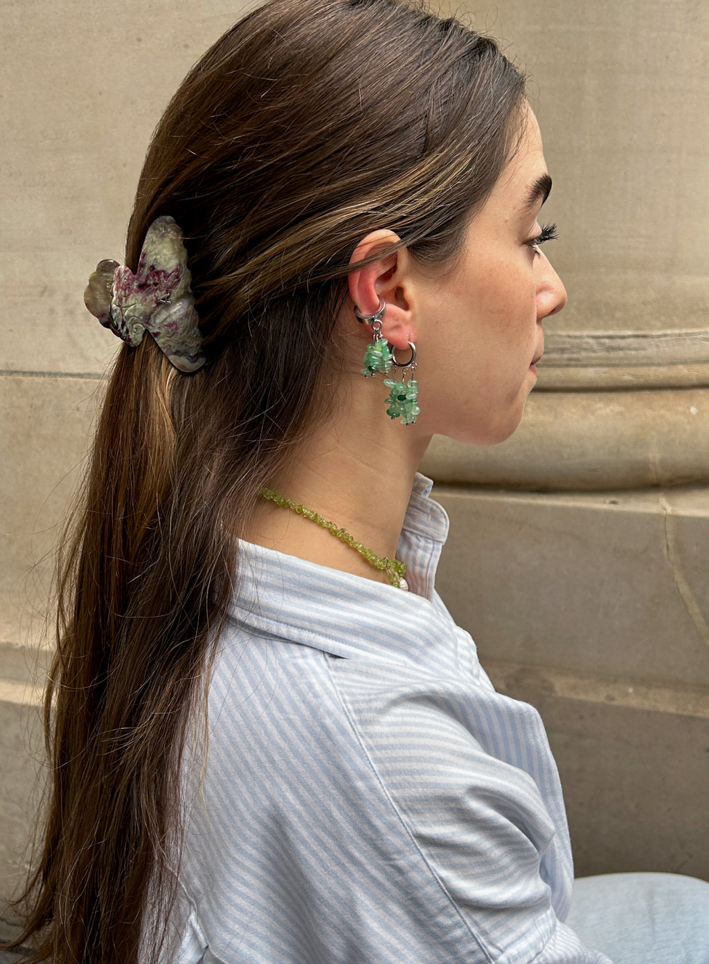 Woman wearing green stone earrings and hair clip against a beige wall.