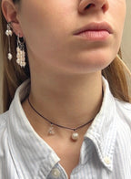 Close-up of a person wearing pearl earrings and a necklace with a small pendant.