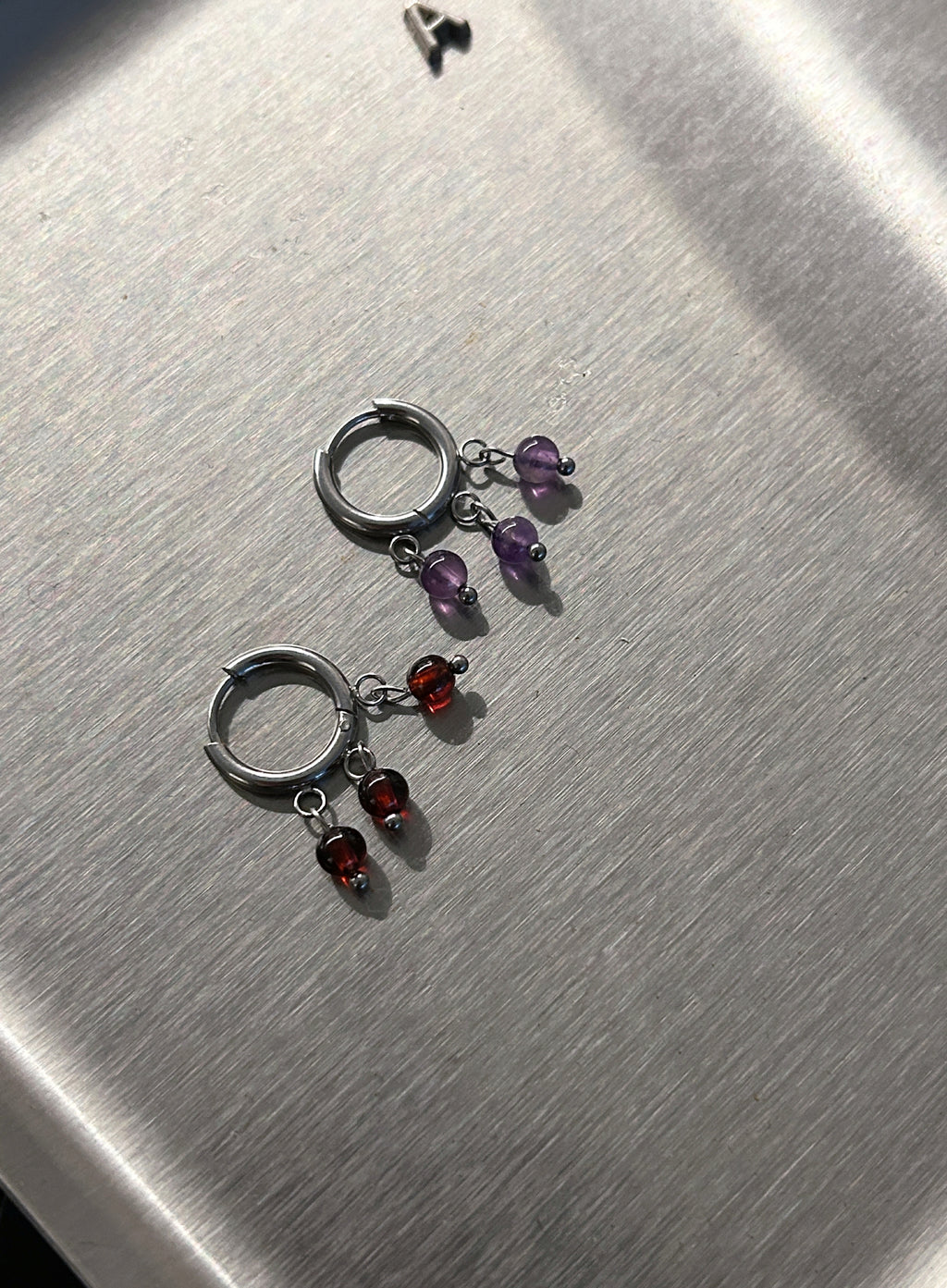 Pair of silver hoop earrings with multicolored gemstones on a metallic surface