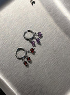 Pair of silver hoop earrings with multicolored gemstones on a metallic surface