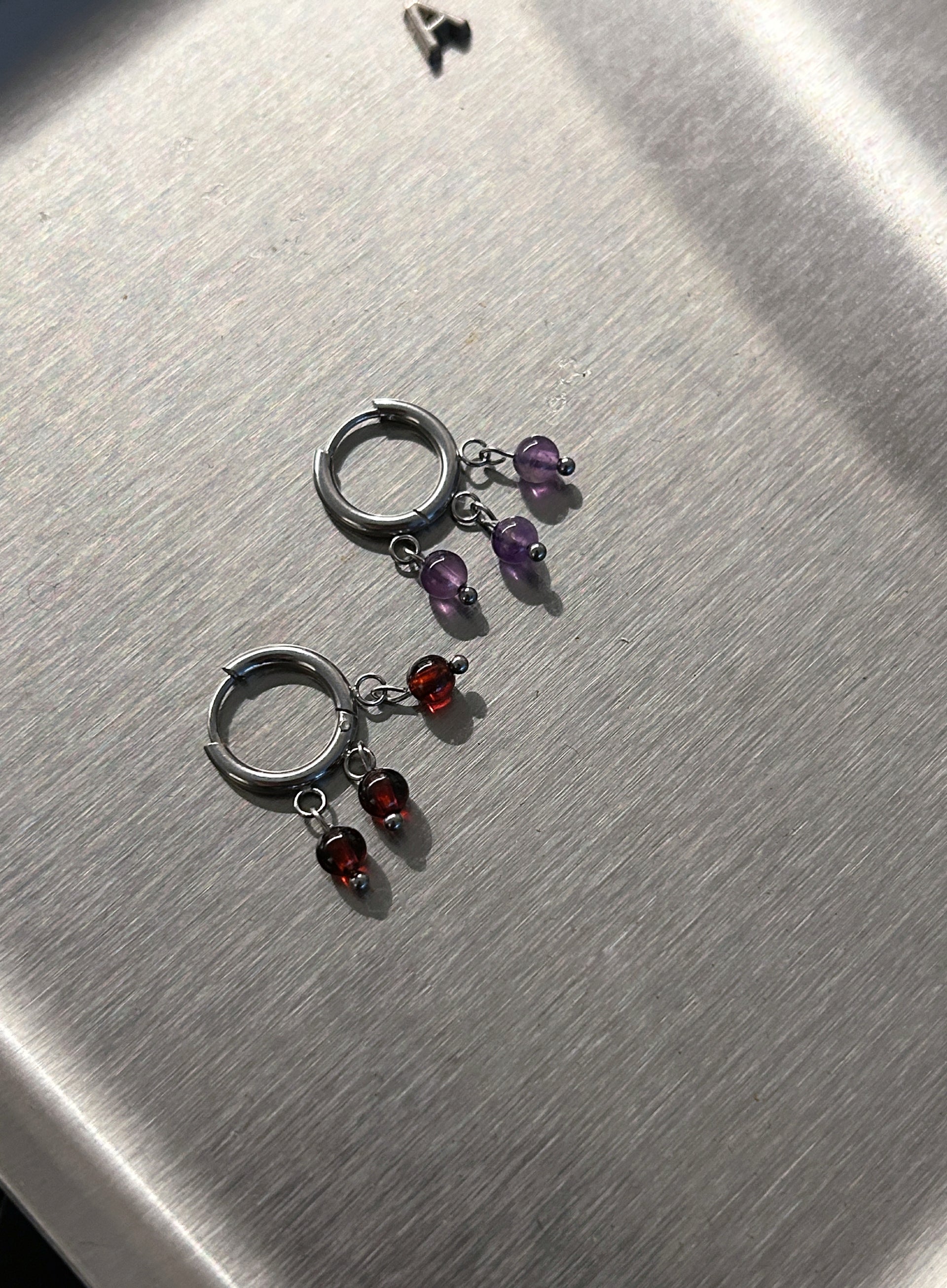 Pair of silver hoop earrings with multicolored gemstones on a metallic surface