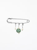 A silver safety pin brooch with three dangling charms: a large green jade bead, a small cream pearl, and a tiny silver bead.