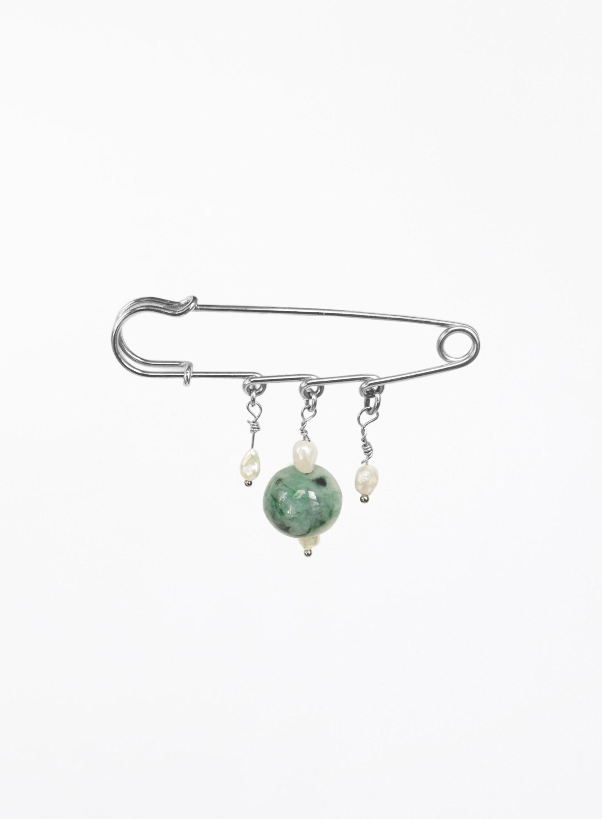 A silver safety pin brooch with three dangling charms: a large green jade bead, a small cream pearl, and a tiny silver bead.