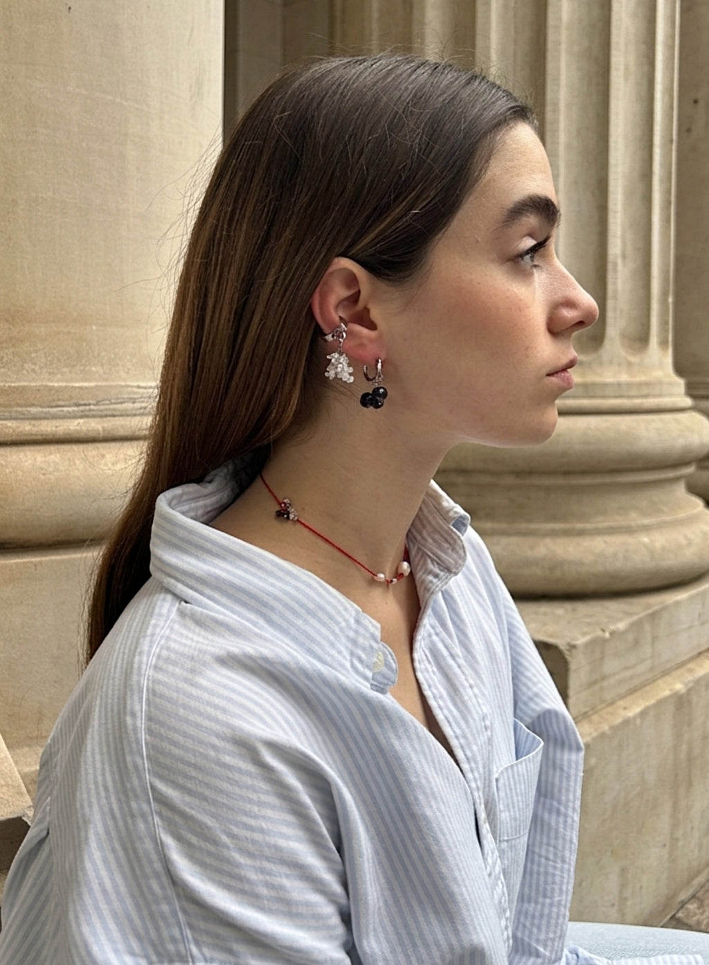 woman in blue stripe shirt waering pearl earrings, ear cuff, and red cord necklace