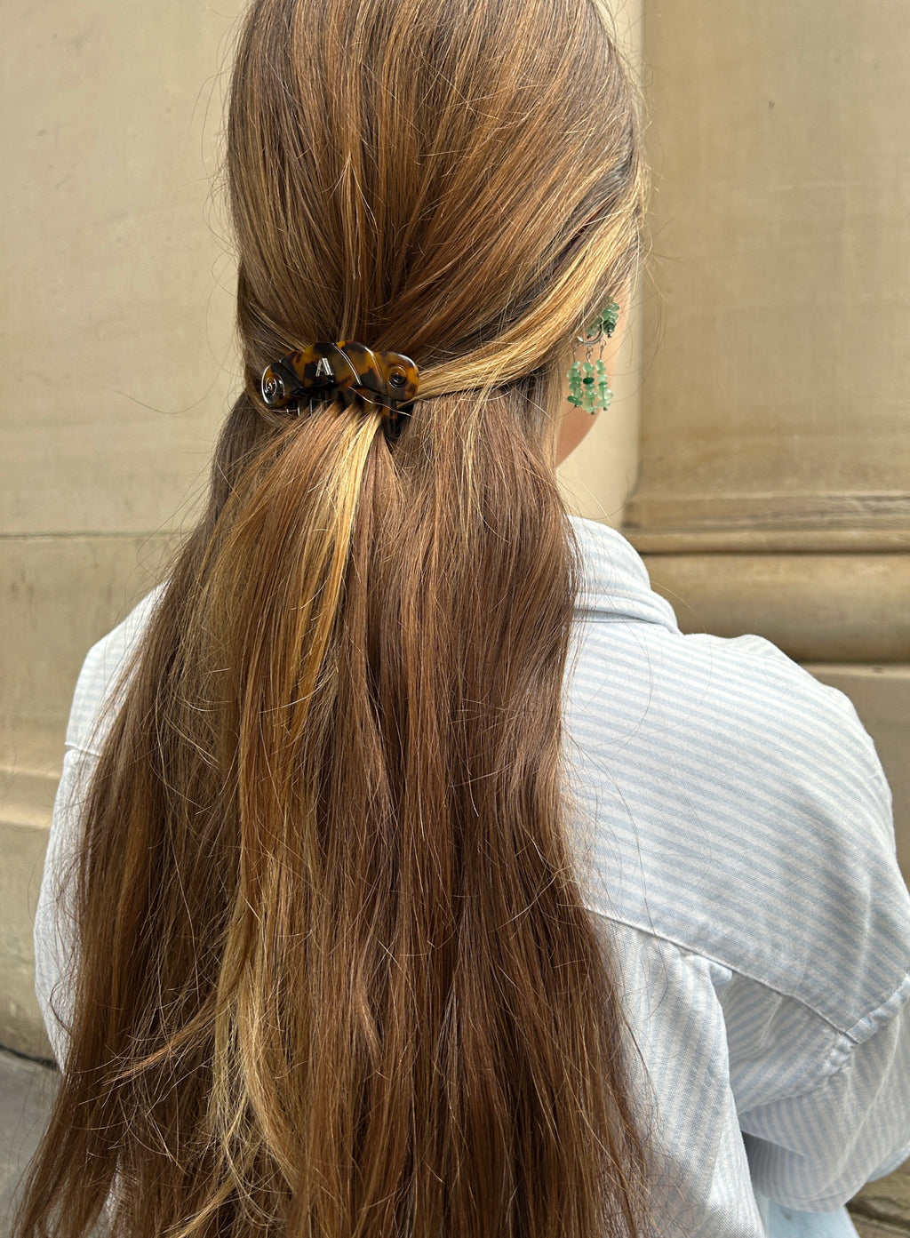 Person with long brown hair tied back with a hair tie, wearing a light blue shirt.