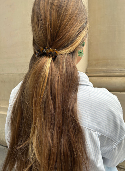 Person with long brown hair tied back with a hair tie, wearing a light blue shirt.
