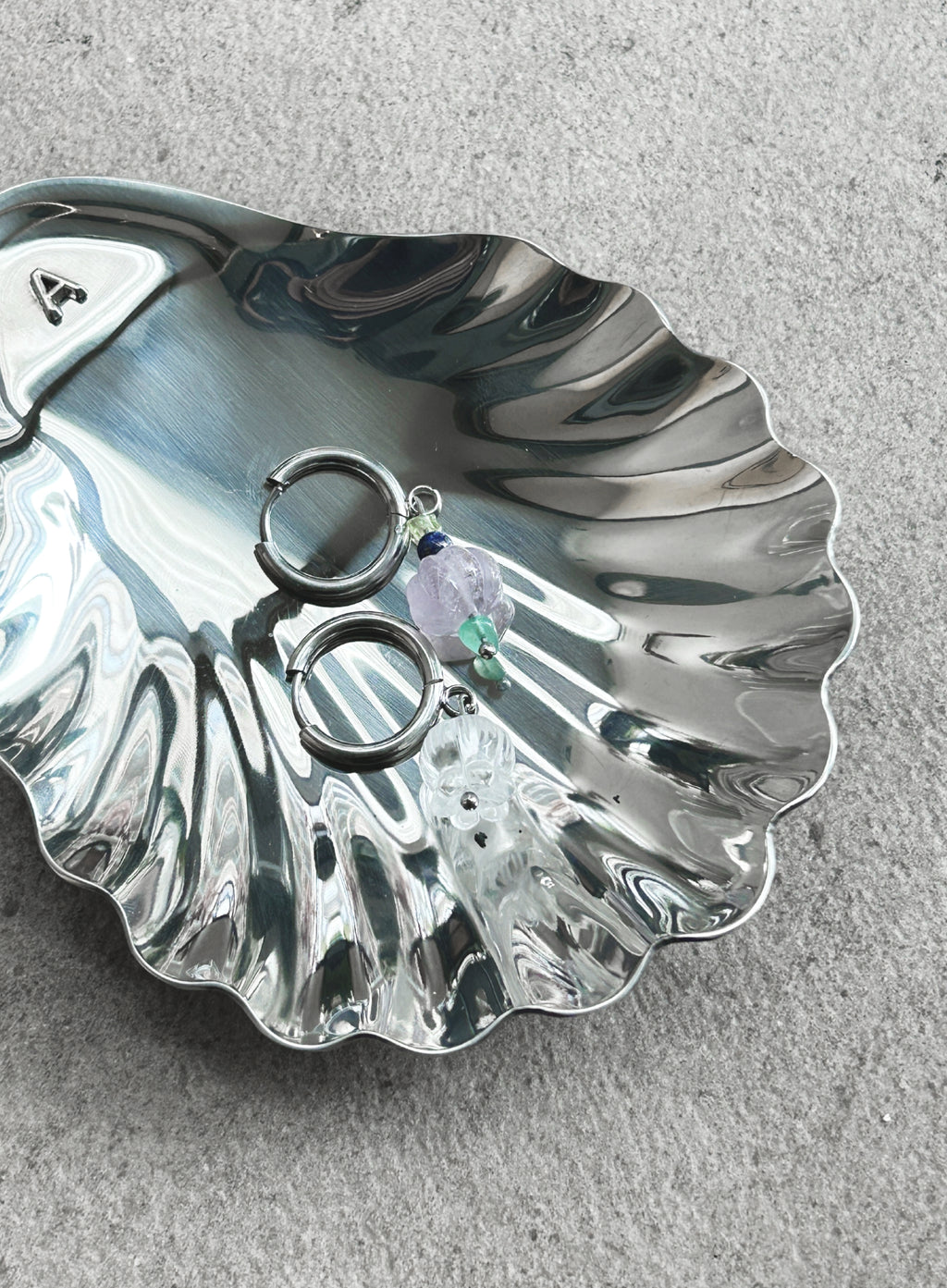 Silver shell-shaped jewelry dish with earrings on a gray surface