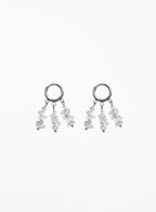 A pair of silver-toned dangle earrings featuring small clear faceted gemstone clusters hanging from open circular hoops, shown against a plain white background.