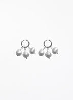 A pair of silver huggie hoop earrings with dangling baroque pearls, shown against a plain white background.