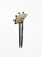 A vintage-style hair pin with a fan-shaped top, featuring a tortoiseshell pattern in amber-brown and black, accented with four small dark pearls at the top.