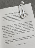 A steel paper-clip bookmark clipped across the top of a book, photographed on a textured gray surface.