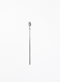 A long, minimalist hairpin featuring a single teardrop-shaped light gray pearl suspended from a very thin, polished silver-toned metal rod, set against a solid white background.
