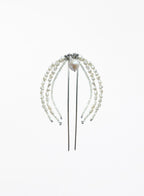 A pearl hair accessory with multiple strands of white freshwater pearls draped over a silver metal hair stick, featuring a central pearl