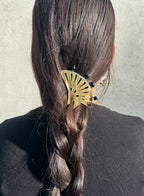A close-up back view of a person with long dark brown hair in a braid, wearing a brown fan-shaped hair accessory with small black pearls.