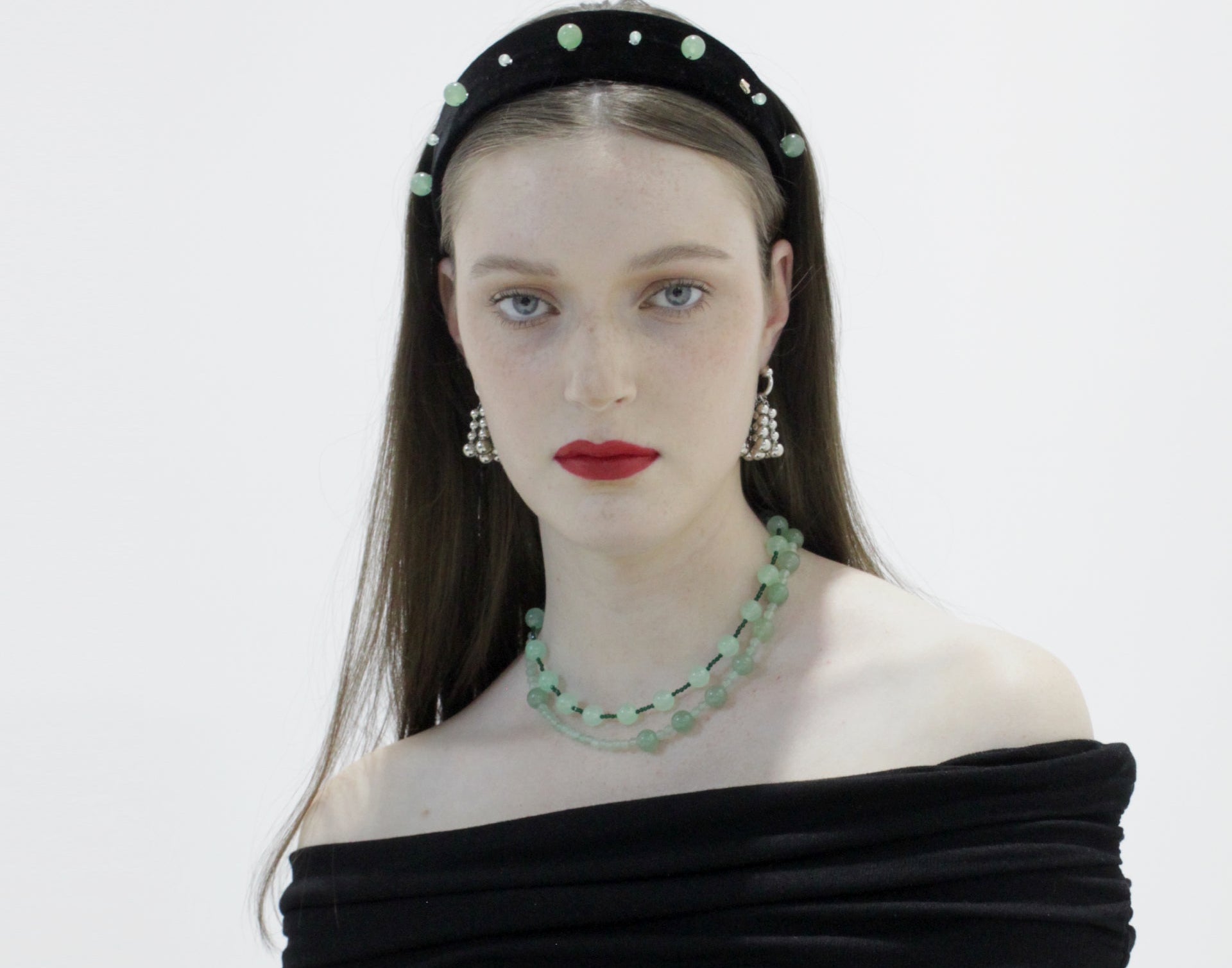 Woman wearing a black off-shoulder dress with green jewelry against a white background