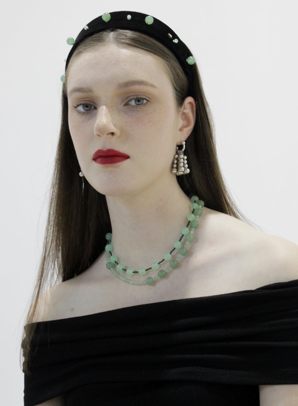 Woman wearing a green beaded necklace and headband with a plain background