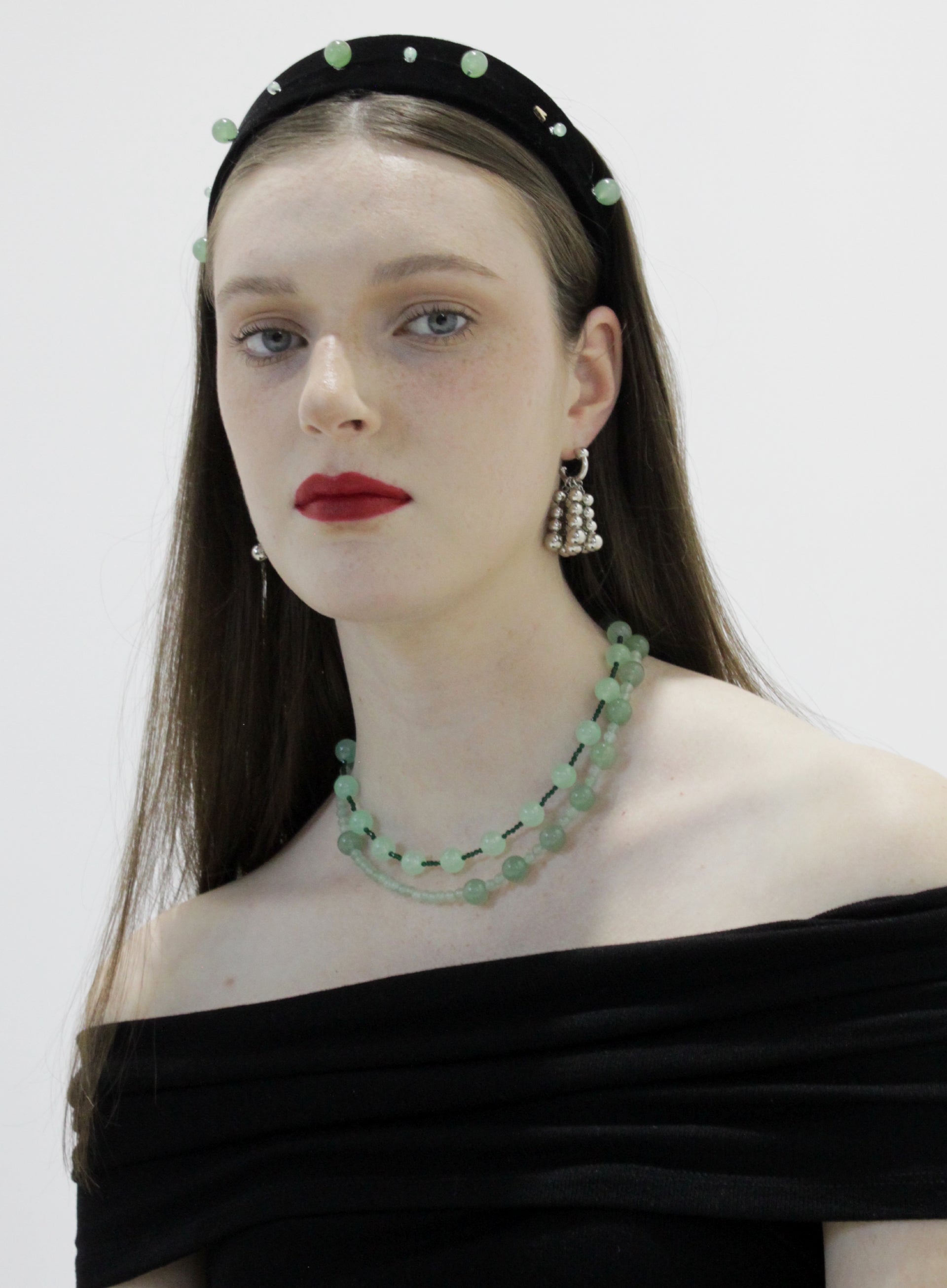 Woman wearing a green beaded necklace and headband with a plain background