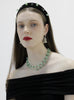 Woman wearing a green beaded necklace and headband with a plain background