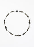 A beaded necklace featuring small white beads alternating with dark gray to black stone chips, finished with a polished silver clasp, shown on a plain white background.