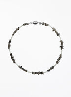 A beaded necklace featuring small white beads alternating with dark gray to black stone chips, finished with a polished silver clasp, shown on a plain white background.