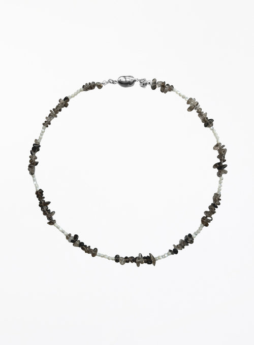A beaded necklace featuring small white beads alternating with dark gray to black stone chips, finished with a polished silver clasp, shown on a plain white background.