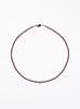 Thin garnet beaded necklace with tear drop charm on a white background