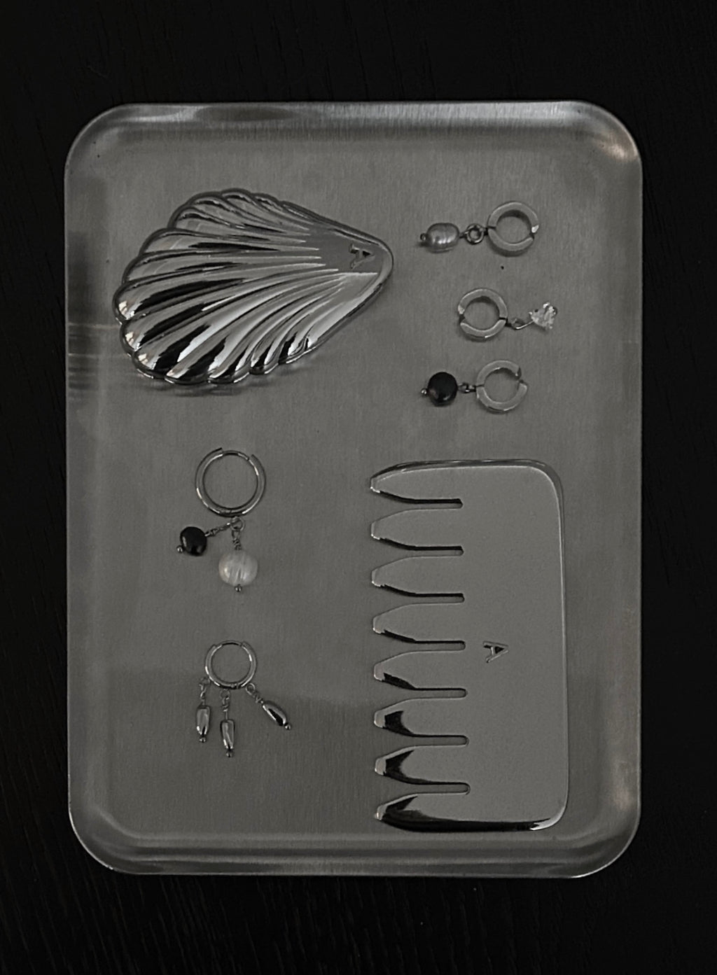 flatlay shot of stainless steel comb massager and multiple earrings with pearls and ear cuffs. also a shell pocket mirror