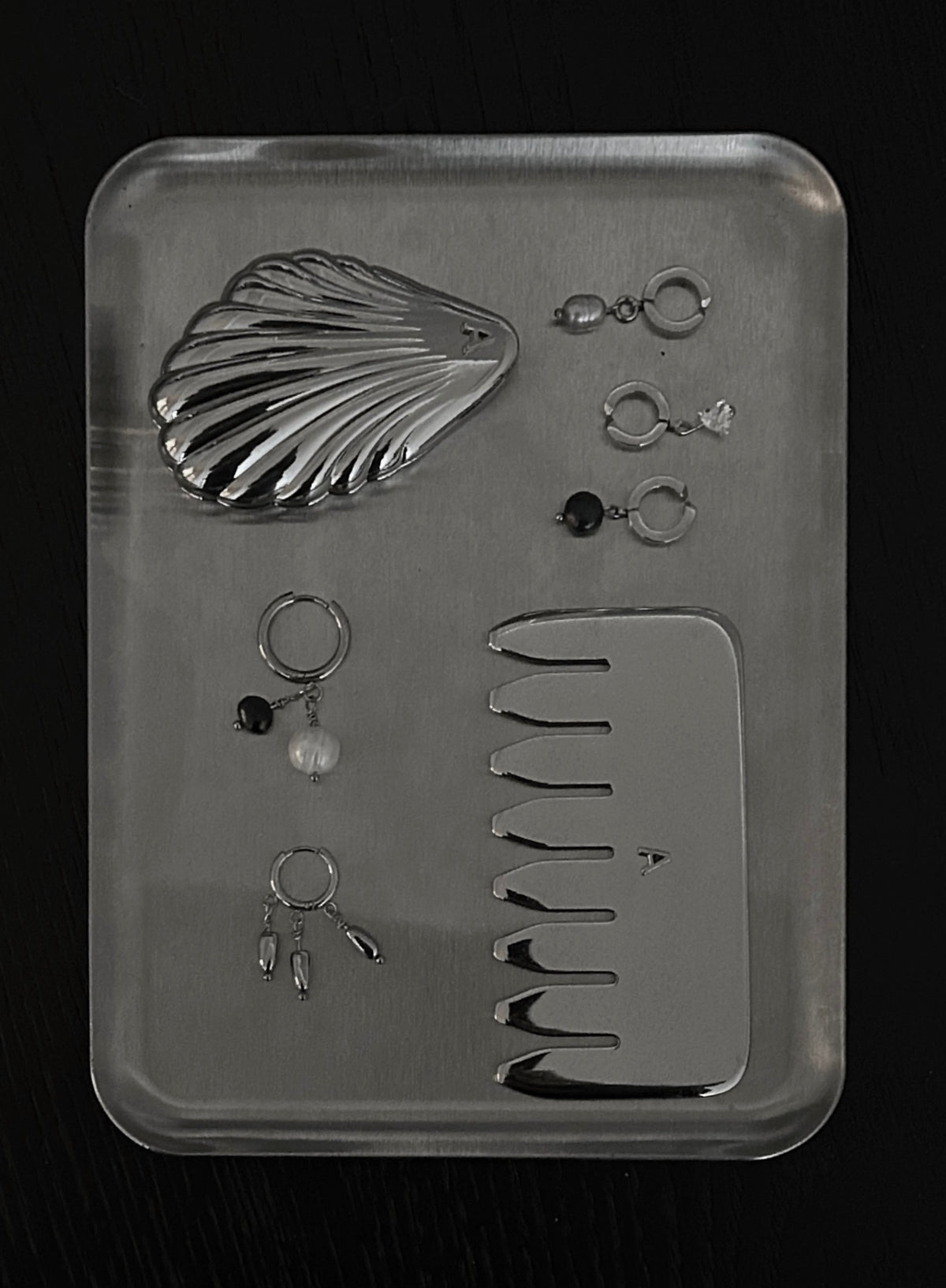 flatlay shot of stainless steel comb massager and multiple earrings with pearls and ear cuffs. also a shell pocket mirror